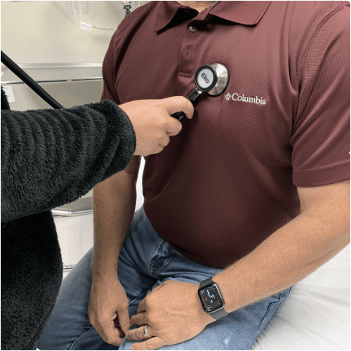 Clinician using an Eko device to listen to heart sounds of male patient wearing a maroon Columbia polo shirt